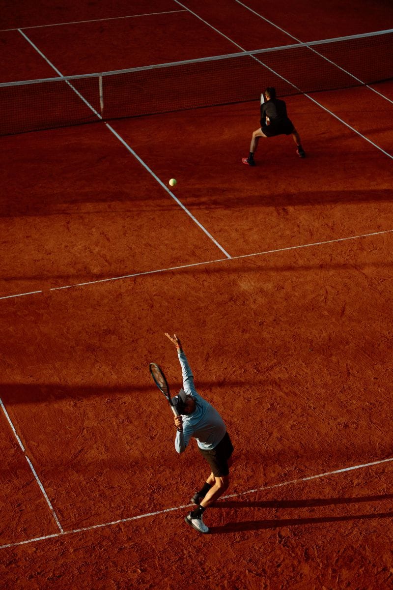 Two tennis players on a clay court illustrating Charles Ellis's concept that investing is a loser's game — won by not making mistakes, not by brilliant shots