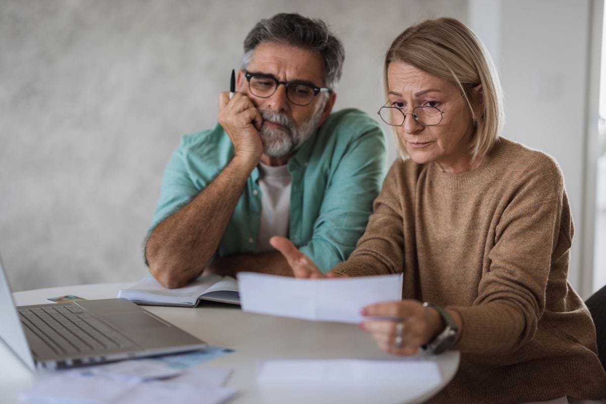 Worried middle-aged couple reviewing financial documents and laptop, concerned about their retirement portfolio and market timing risk