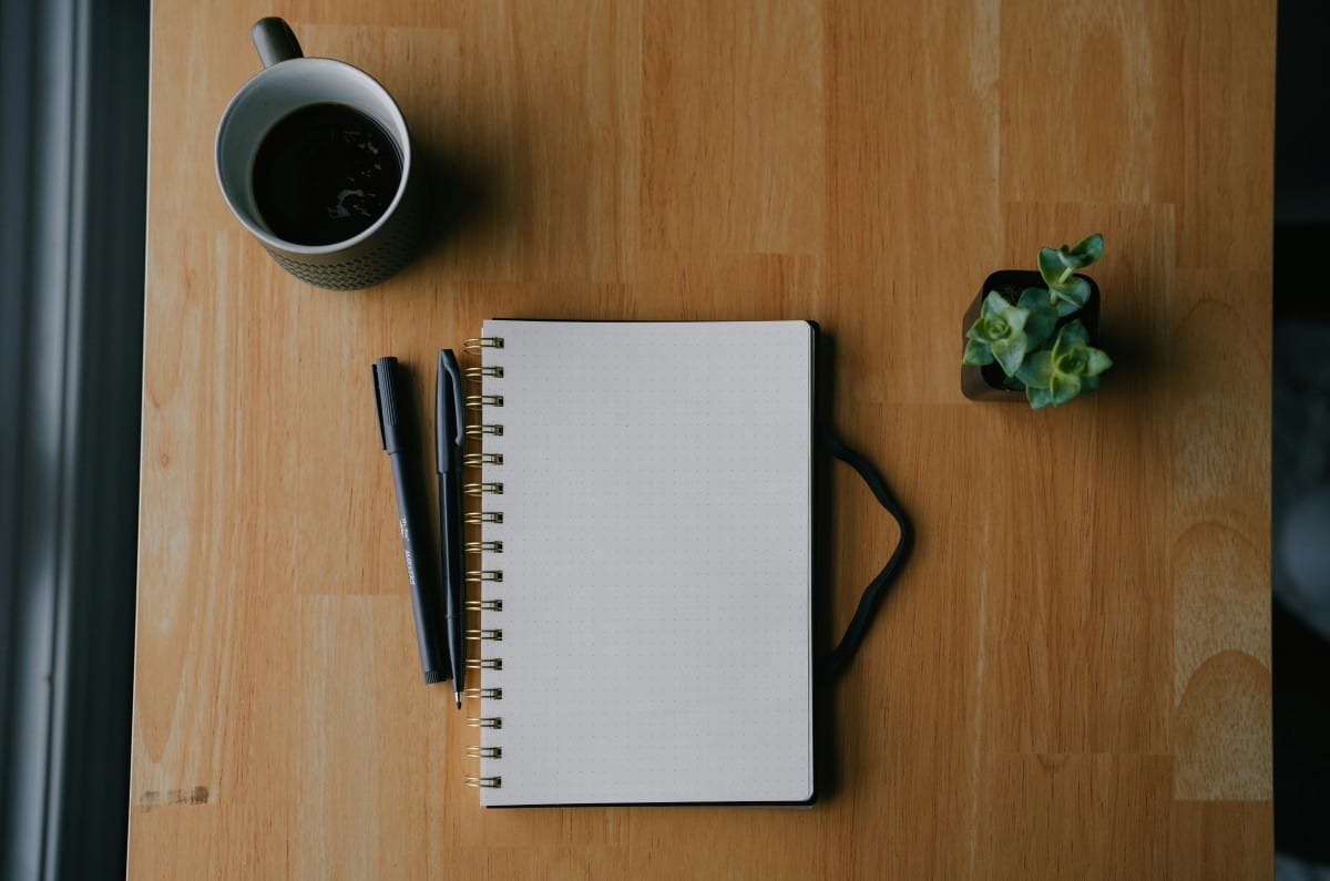 Open blank notebook with pen and coffee on a wood desk — illustrating careful retirement planning and IRA strategy review.